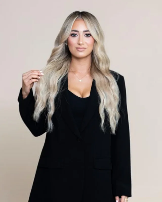 Portrait of Sam with long dimensional blonde waves in a black blazer, Specialty Stylist for blonding and weft hair extensions at Infinite Hair Studio in Baton Rouge, LA